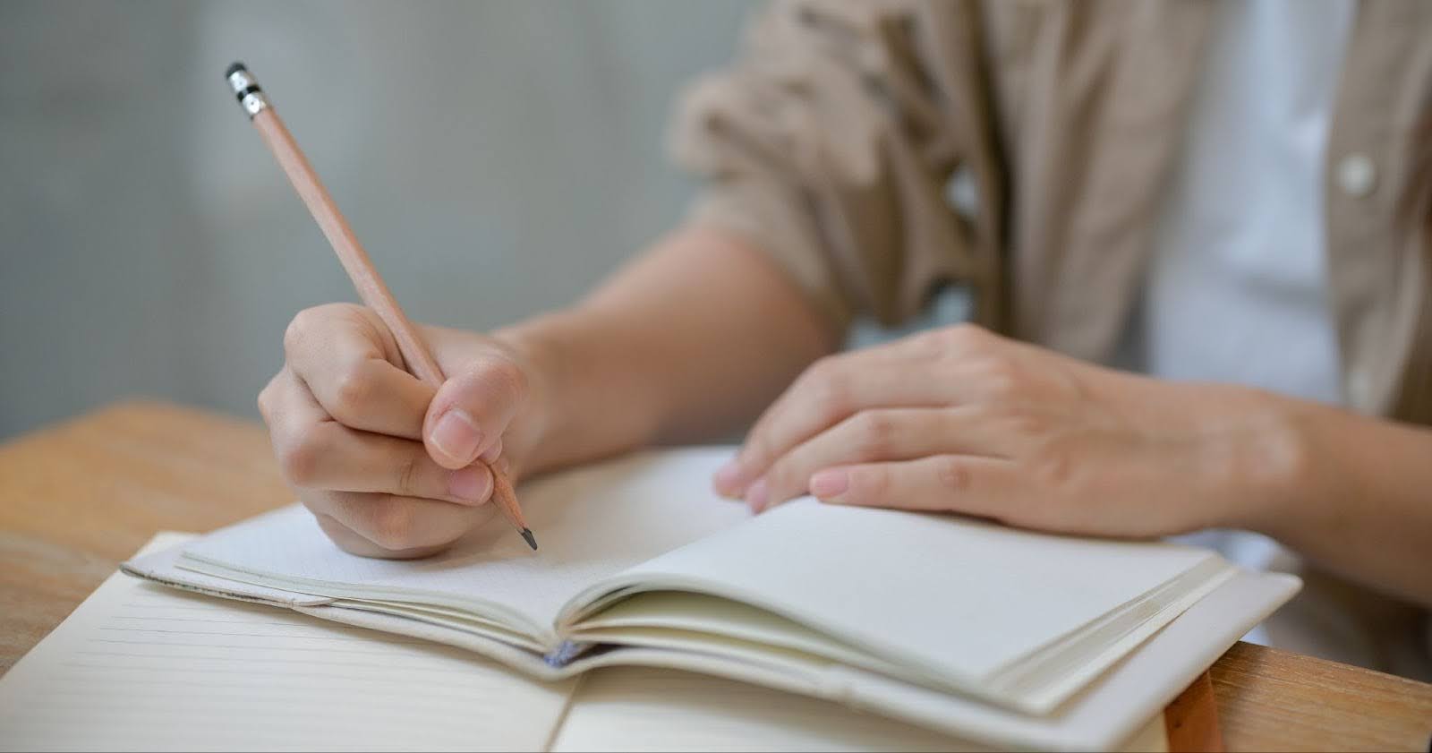 鉛筆を持ち机に広げたノートに何か書いている人