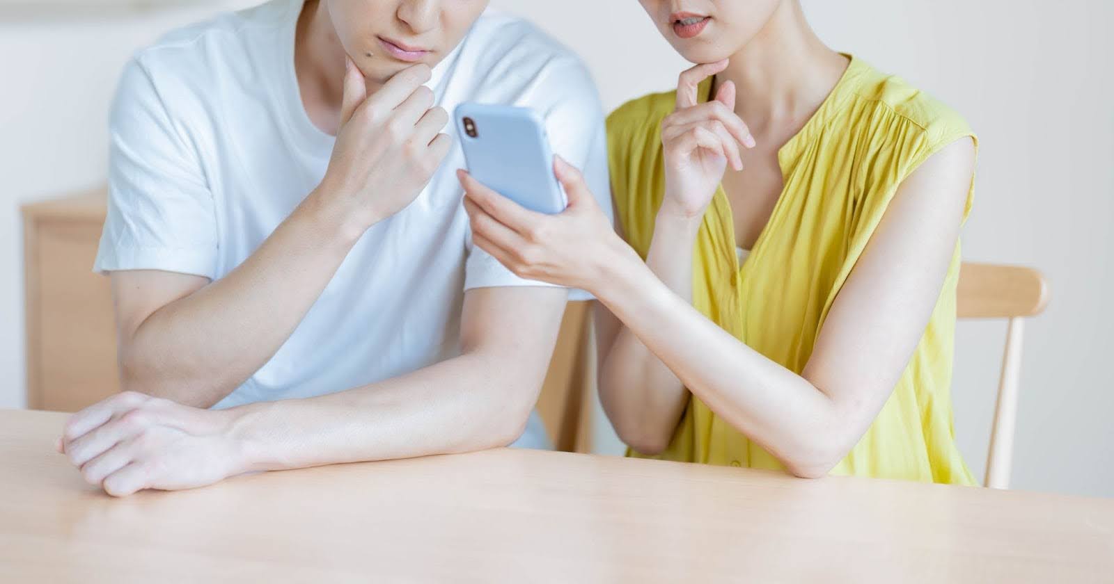 黄色の服の女性白Tシャツの男性がスマホを見ながら相談している写真