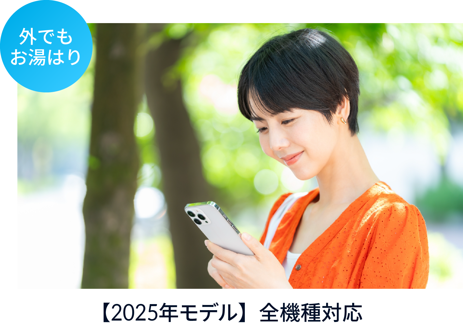 晴れた屋外、木々を背景にスマホを操作して微笑むショートカットにオレンジのカーディガンの女性。「外でもお湯はり。2025年モデル全機種対応」